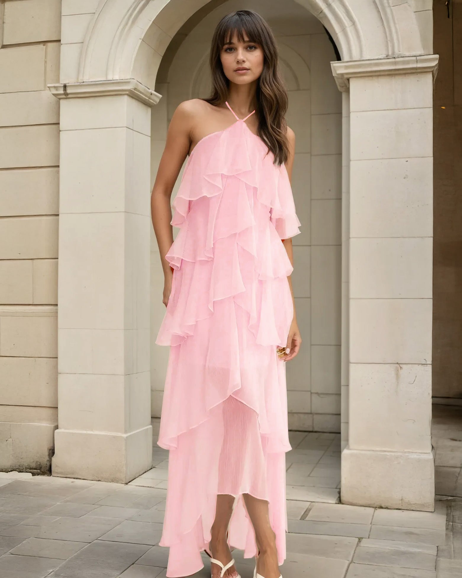Woman wearing a pink ruffled dress standing in front of a stone archway.