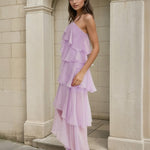 Woman wearing a lilac one-shoulder dress standing against a stone archway.