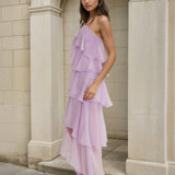 Woman wearing a lilac one-shoulder dress standing against a stone archway.