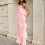Woman wearing a pink ruffled dress standing against a light-colored wall.