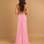 A woman viewed from the back wearing a floor-length pink gown with a draped, gathered back and a slight train, standing against a warm tan studio backdrop.