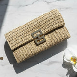 Woven handbag with a decorative clasp on a marble surface with a white orchid and gold bracelet.