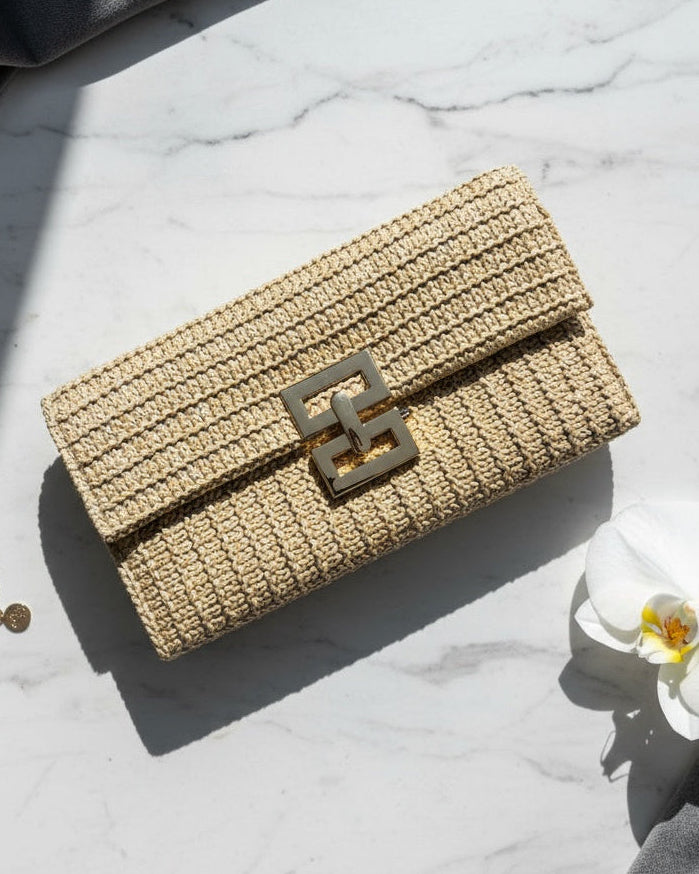 Woven handbag with a decorative clasp on a marble surface with a white orchid and gold bracelet.