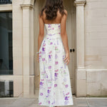 Woman wearing a strapless floral Broderie midi dress standing in front of a stone archway.