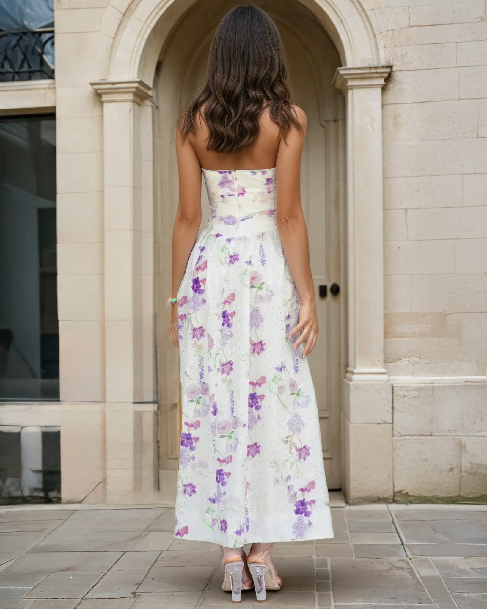 Woman wearing a strapless floral Broderie midi dress standing in front of a stone archway.