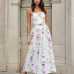 Woman wearing a strapless floral Broderie midi dress standing in front of a stone archway.