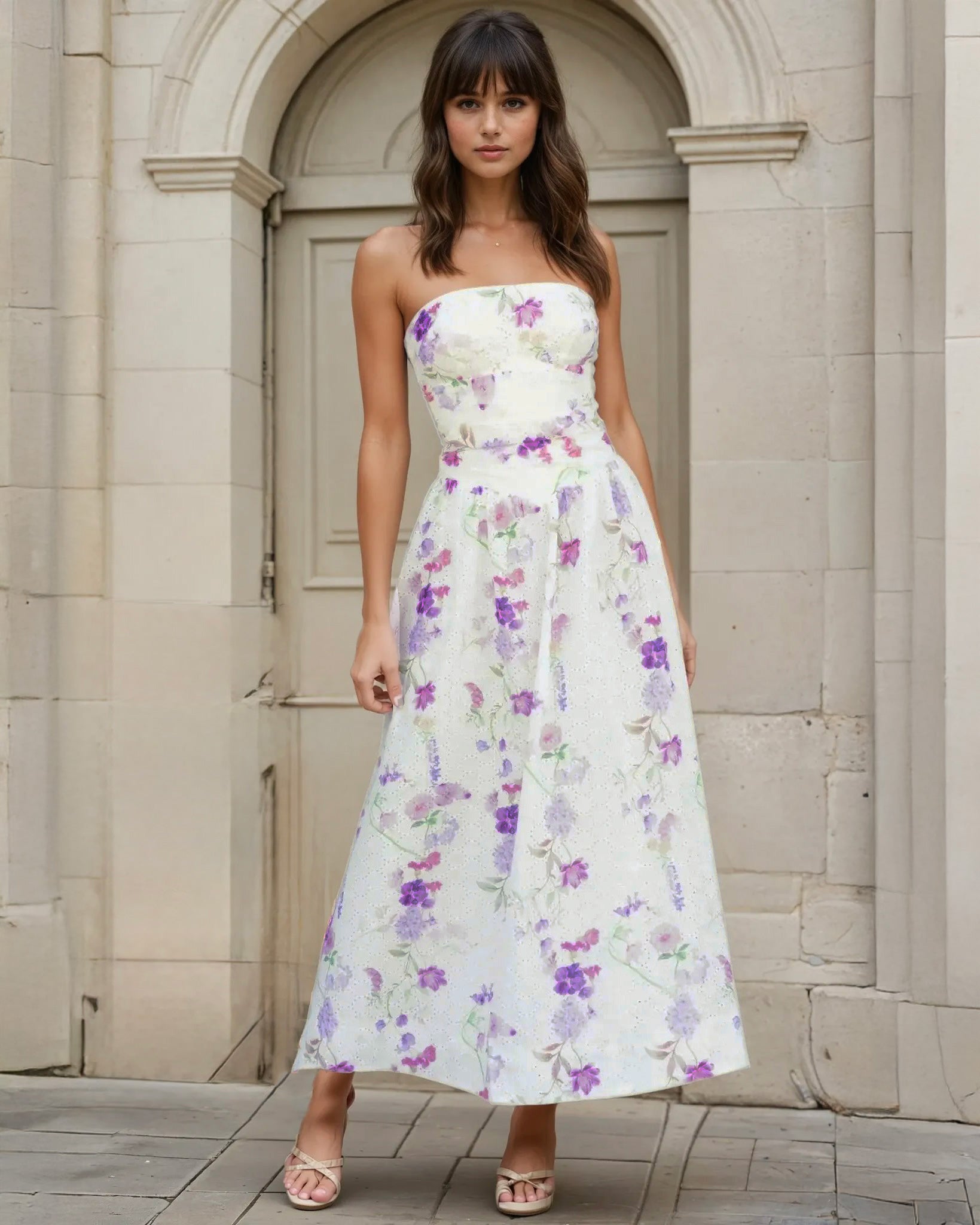 Woman wearing a strapless floral Broderie midi dress standing in front of a stone archway.